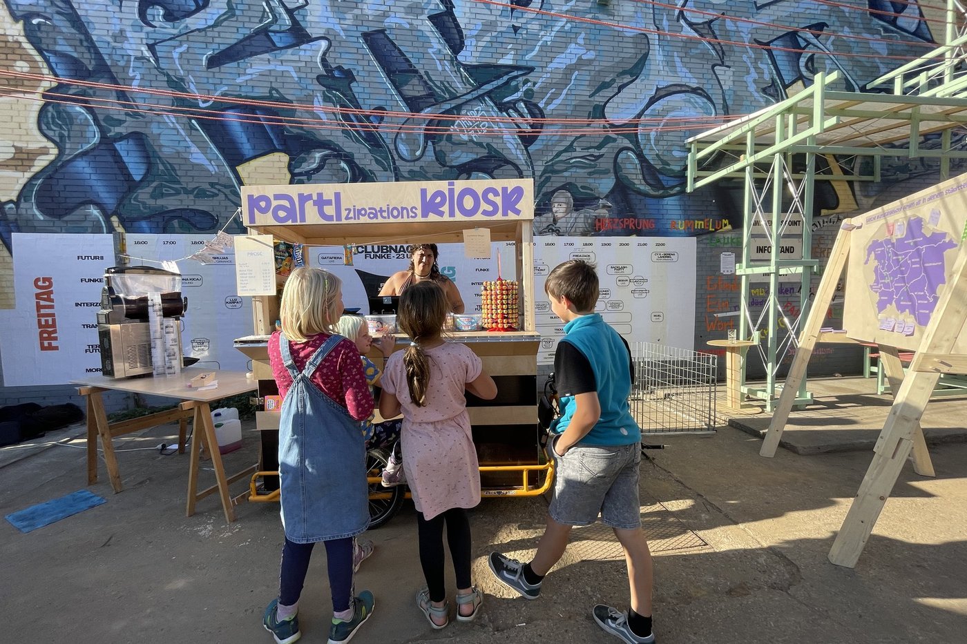 Vier Kinder stehen vor einem Kiosk-Stand an dem Süßigkeiten verkauft werden