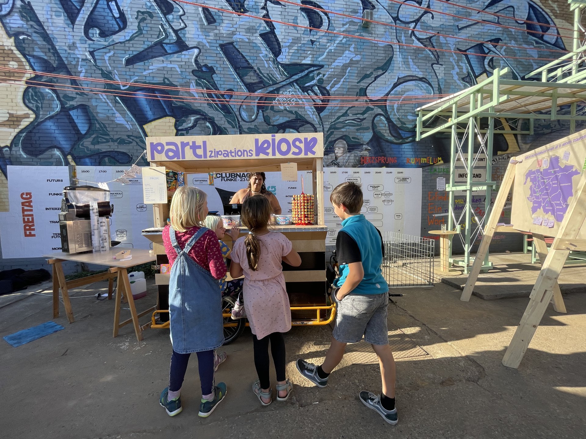 Vier Kinder stehen vor einem Kiosk-Stand an dem Süßigkeiten verkauft werden
